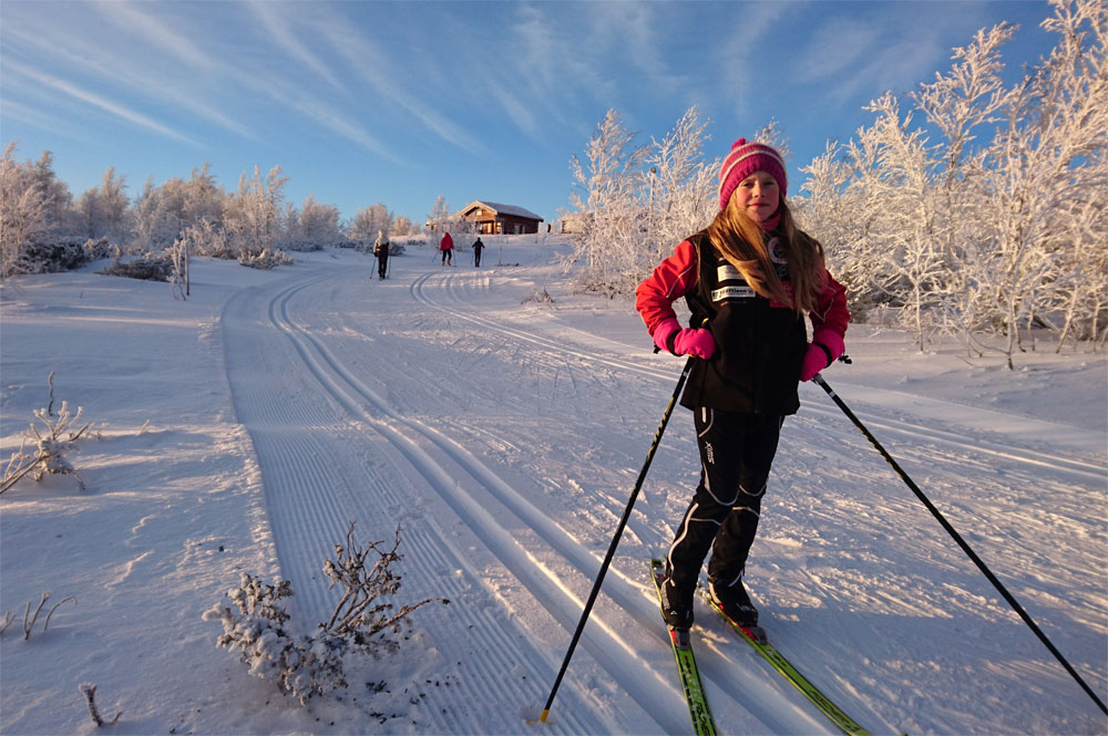 Et barn står og posere med ski på beina i et skispor
